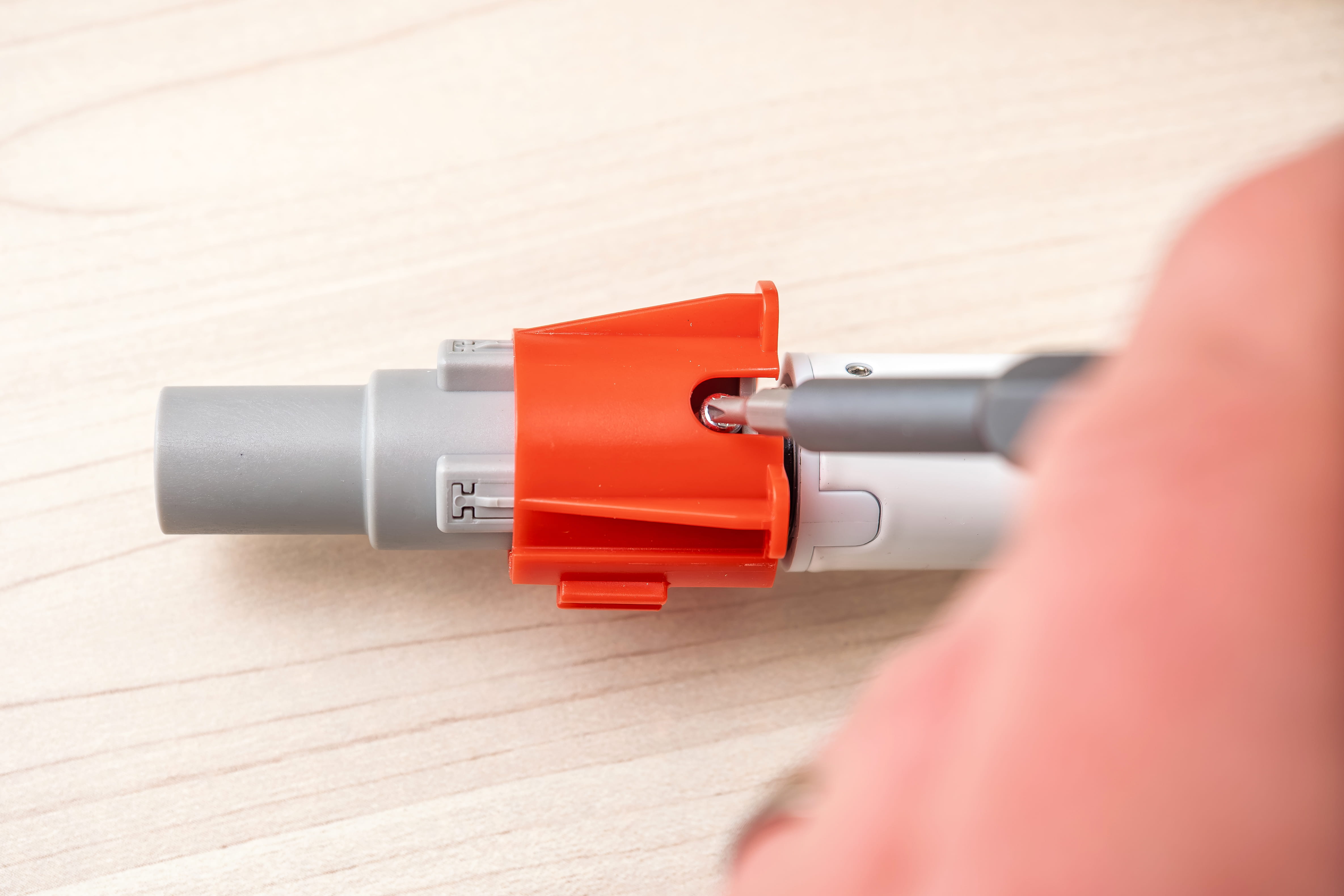 Hand holding a gray tube with a red plastic clamp on a wooden surface