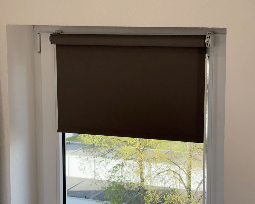 Partially lowered dark roller blind with Eve Motionblinds motor on a white-framed window